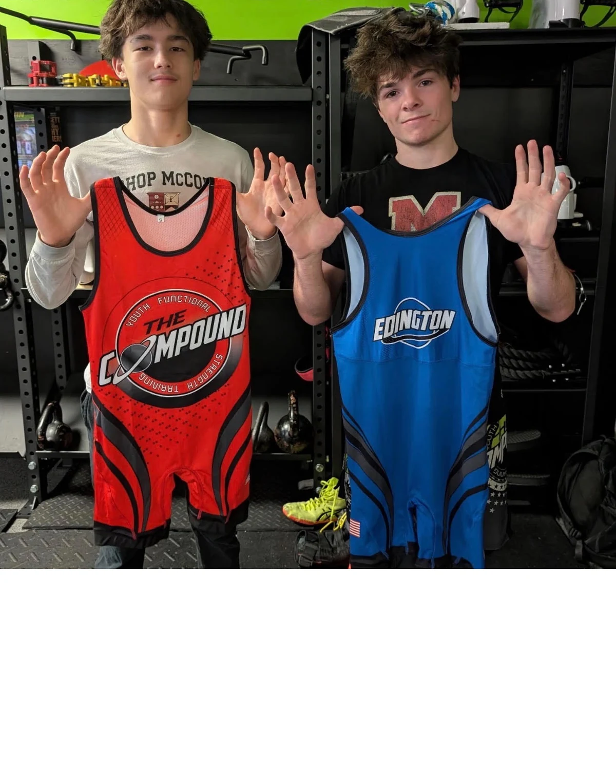 Photo shared by Trip Edington on Facebook: two teenage wrestlers in a gym, each holding up a finished singlet — one red with the Compound crest, one blue lettered EDINGTON.